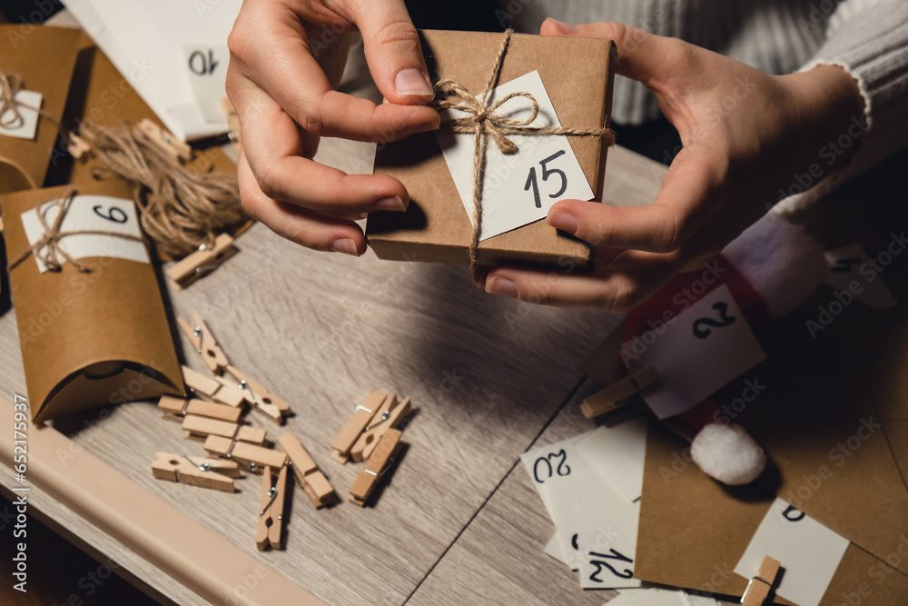 Obraz premium Unrecognizable young woman sticks number on craft bag, fastens with clothespin. Female making kraft paper for homemade advent calendar Made with your own hands step by step DIY crafts do it yourself