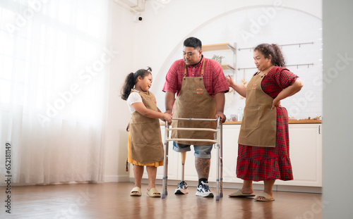 A plus-size family with a father wearing a prosthetic leg, Daughter helps father walk with walker in the kitchen room of the house