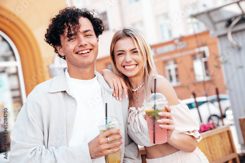 Young smiling beautiful woman and her handsome boyfriend in casual summer clothes. Happy cheerful family. Female having fun. Couple posing in street. Holding and drinking cocktail drink in plastic cup