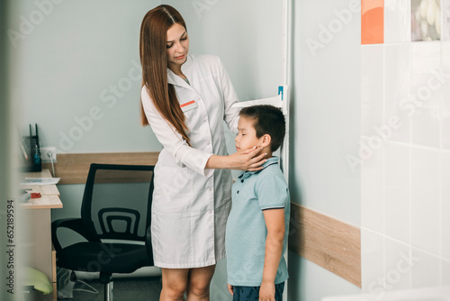 Female doctor measuring boy's height at medical clinic photo
