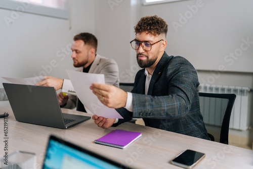 Portrait of young businessman reading contract document, preparing to sign a contract of sale, thinking considering risks, analyzing financial report at office table. Executive checking legal document
