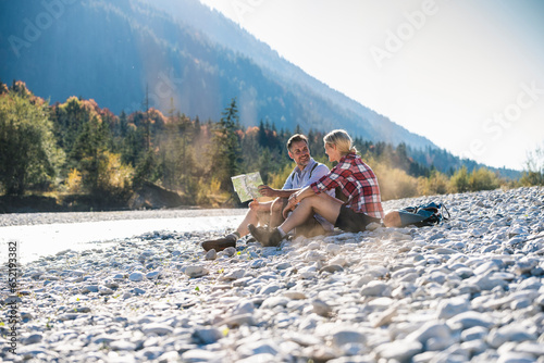 Austria, Alps, couple on a hiking trip having a break at a brook reading map photo