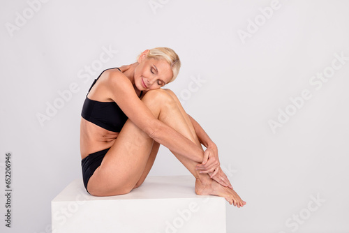 Full body cadre of satisfaction nice old woman hugging her perfect skin flawless epilator legs no hair isolated on gray color background