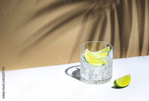 Ti punch cocktail drink with white rum agricole, sugar syrup and lime, traditional Caribbean beverage. Beige background, palm leaves shadow, copy space
