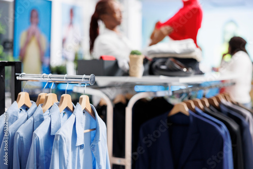 Formal shirts and jackets hanging on display rack showcasing latest arrival merchandise in retail shopping mall with blurred background. Apparel on hangers in fashion boutique close up