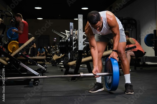 Strong Hispanic man removing weight plate on barbell after deadlift at a gym.