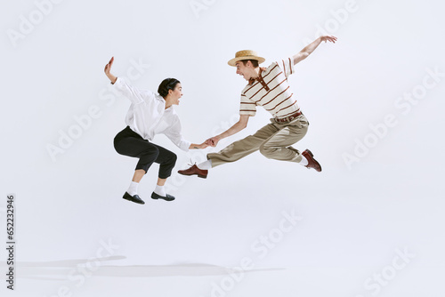 Happy, attractive young man and woman in stylish vintage clothes dancing lindy hop isolated on white studio background. Concept of art, hobby, retro dance style, choreography, beauty. Ad photo