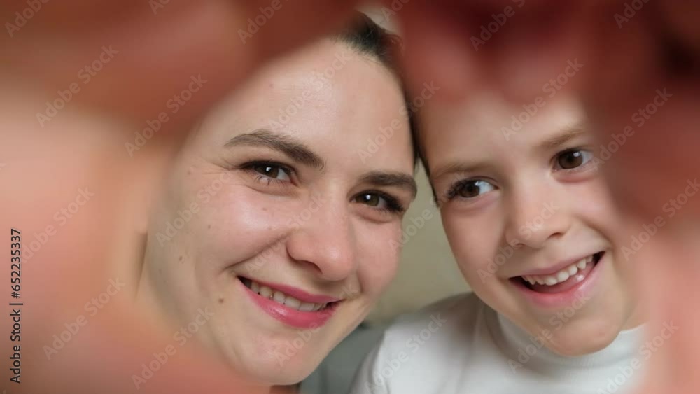 A mother and a young son look at the camera through a heart made from their hands. Love of mother and child, mother's day