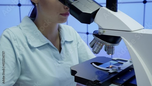  Young woman technician is examining a histological sample of a biopsy in the laboratory research