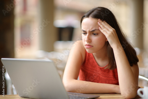 Worried woman checking laptop content in a restaurant photo