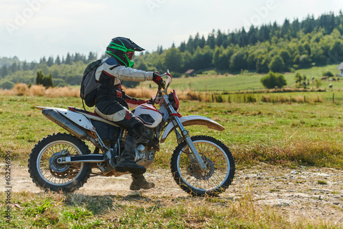 A professional motocross rider exhilaratingly riding a treacherous off-road forest trail on their motorcycle.