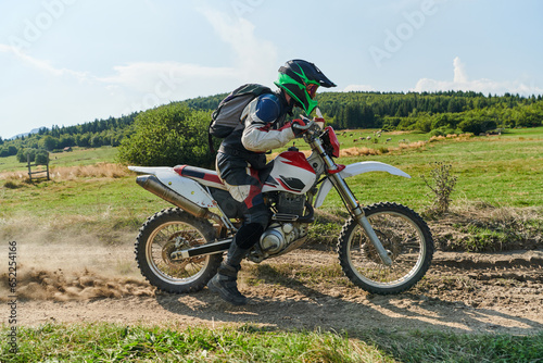 A professional motocross rider exhilaratingly riding a treacherous off-road forest trail on their motorcycle.