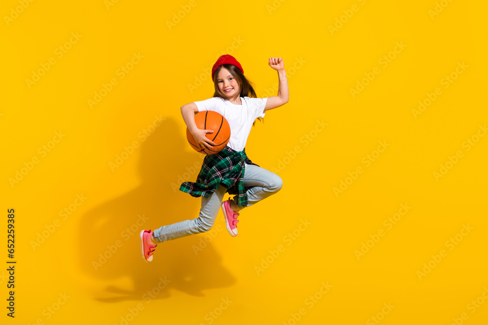 Full length photo of charming little girl run jump raise fist basketball ball wear trendy white garment isolated on yellow color background