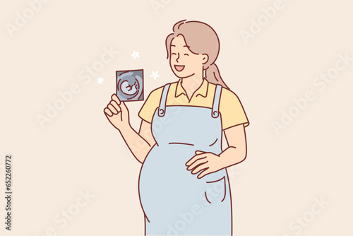 Pregnant woman holds ultrasound picture and laughs rejoicing at imminent birth of son or daughter