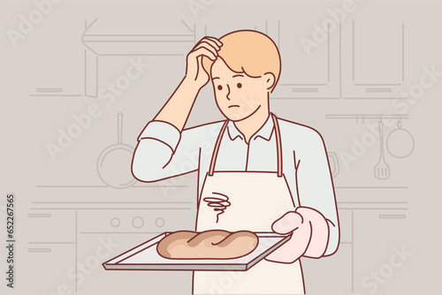 Confused baker holds tray with spoiled bread, burnt due to non-compliance with cooking technology