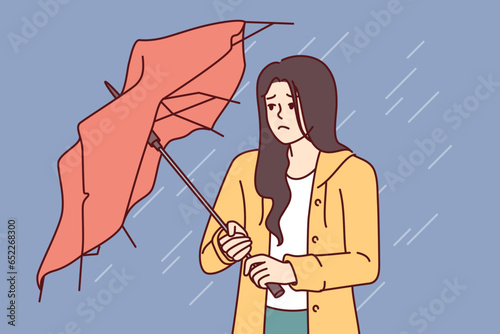 Wet woman stands with broken umbrella in heavy rain, and is sad because of cold and strong wind. Upset girl walking down street during storm and autumn rain needs waterproof clothes