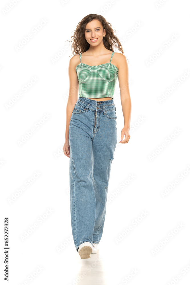 Full length shot of smiling young smiling woman wearing green shirt and blue jeansi while walking at isolated white background. Full length shot of smiling young smiling woman wearing green shirt and blue jeansi while walking at isolated white background.