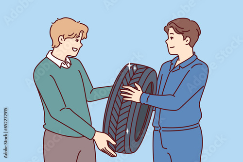 Man buys new tires for car wheel and consults mechanic, who help make right choice. Casual guy purchases winter tires for wheels to protect himself and those around from car accident.