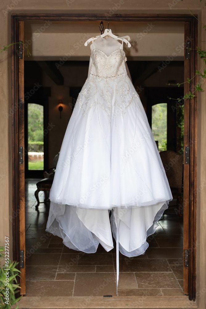 a wedding dress hanging in the doorway of a house with a bouquet