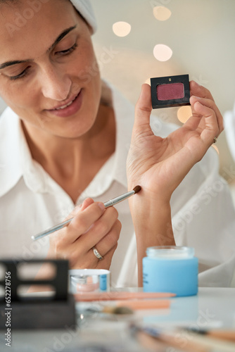 Smiling woman testing eyeshadow on hand