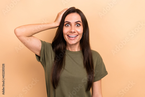 Photo of astonished woman with straight hairdo dressed khaki t-shirt arm on head impressed staring isolated on beige color background