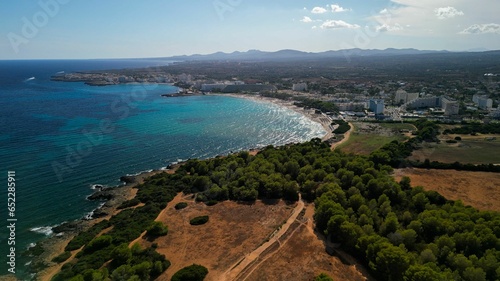 Drone shot of a stunning beach in Spain, featuring beachfront structures and sailing boats