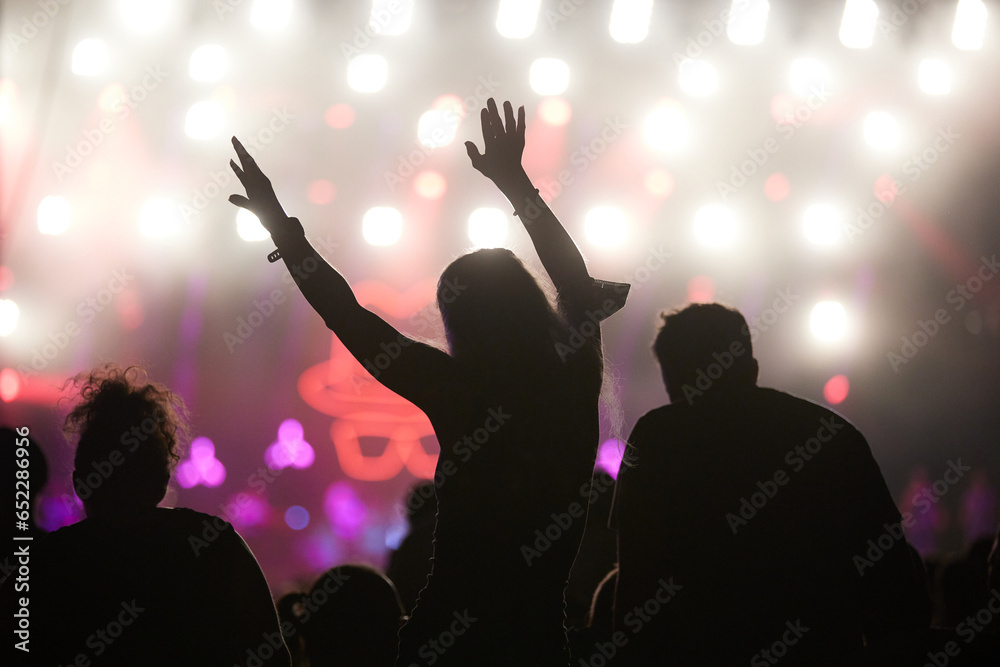 Silhouettes of people dancing during at a concert with the illuminated colorful stage on background