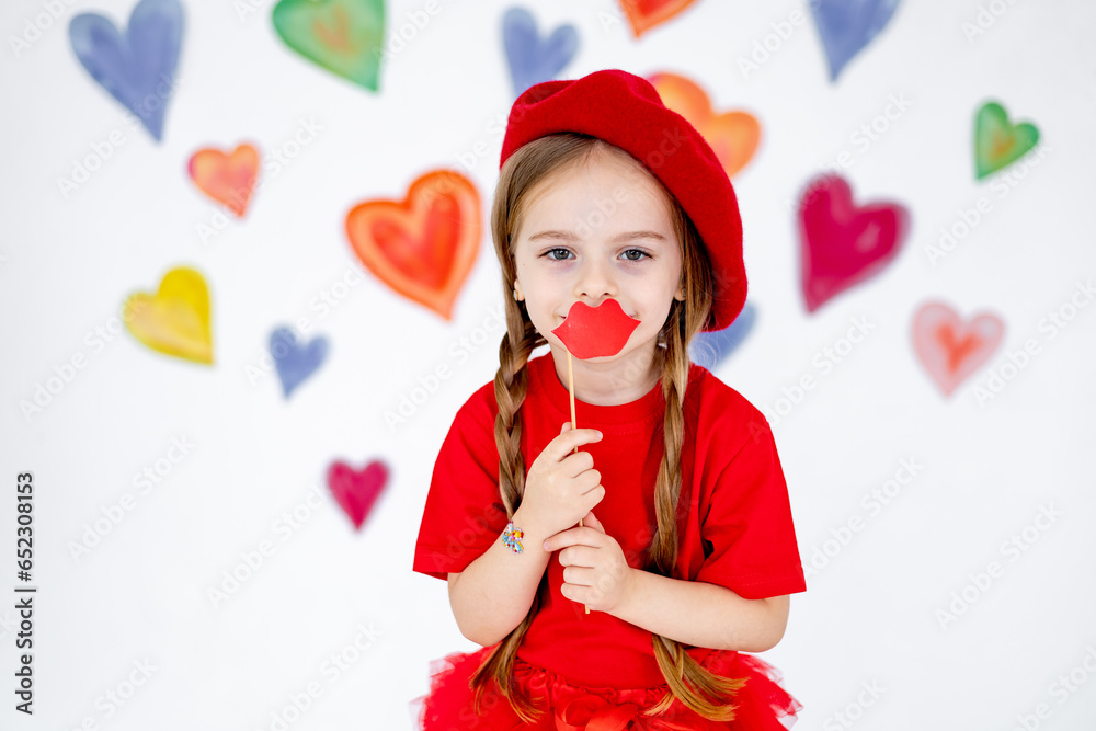 portrait of a little girl in a red beret and clothes on a background of colorful hearts sends an air kiss, a smiling child, the concept of valentine's day and love