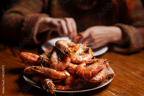 Large cooked king prawns on the table. An unrecognizable man is eating shrimp at the table.