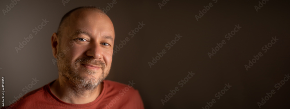 Unshaven middle-aged man, about 40 years old, wearing approachable smile and ordinary look in close-up shot. Banner, space for text. - obrazy, fototapety, plakaty 