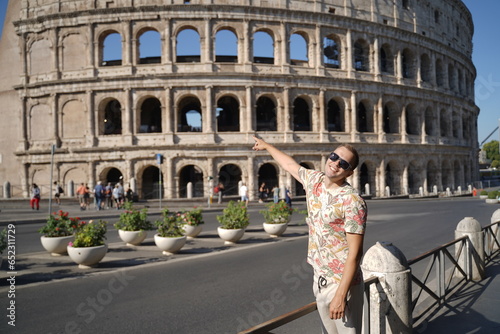 A young man wearing glasses points to the Colosseum in Italy. Vacation.