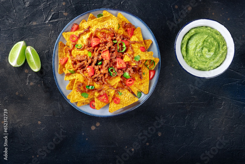 Nachos, Mexican food, tortilla chips with beef and fresh vegetables, overhead shot on a black background with copy space