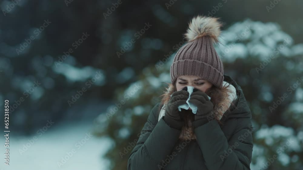unhappy modern woman in green coat and brown hat outdoors in the city park in winter with mittens, napkin blowing nose and beanie hat. unhappy modern woman in green coat and brown hat outdoors in the city park in winter with mittens, napkin blowing nose and beanie hat.