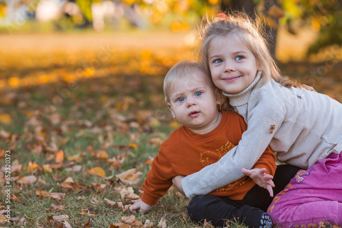 Portrait of a little boy 9 months old and a girl 4 years old outdoors. Happy children are playing in the autumn park. Sister hugs brother. Happy childhood and motherhood.