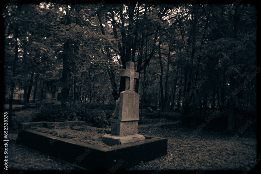 The old film photo depicts a creepy grave cross standing in the middle ...