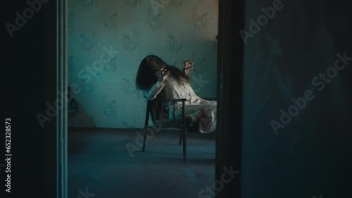 Creepy woman with long unkempt hair writhing in armchair, possessed by devil