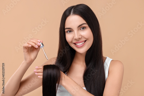 Beautiful woman applying hair serum on beige background. Cosmetic product