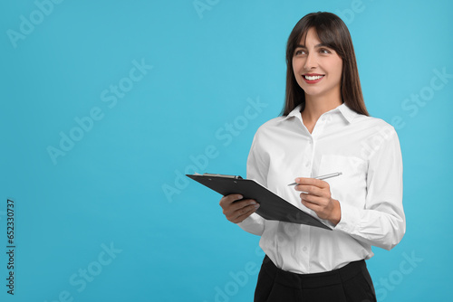 Happy secretary with clipboard and pen on light blue background. Space for text