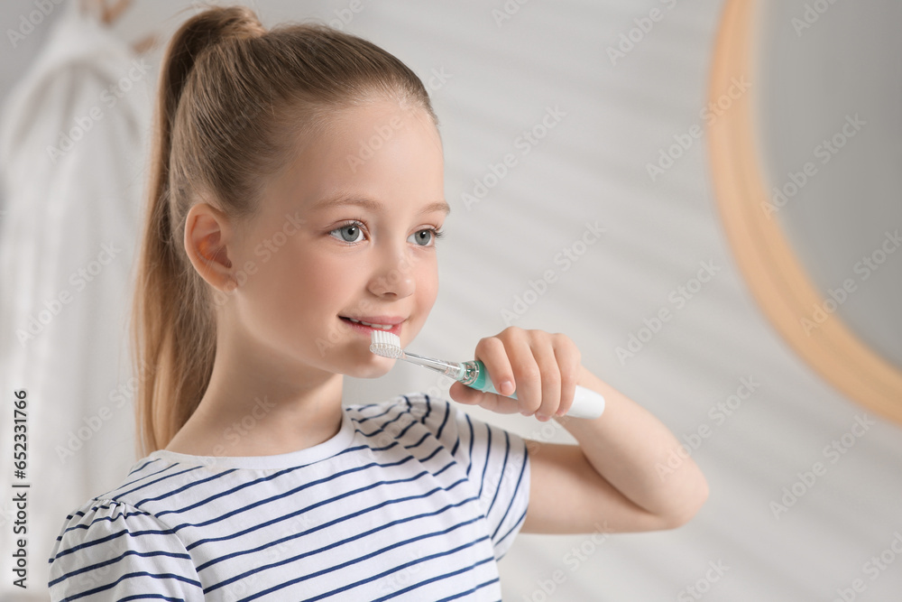 Cute little girl brushing her teeth with electric toothbrush near mirror in bathroom, space for text Cute little girl brushing her teeth with electric toothbrush near mirror in bathroom, space for text