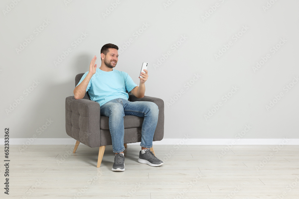 Happy man sitting in armchair and having video chat via smartphone indoors, space for text