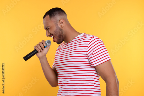 Handsome man with microphone singing on orange background