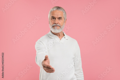 Senior man welcoming and offering handshake on pink background © New Africa