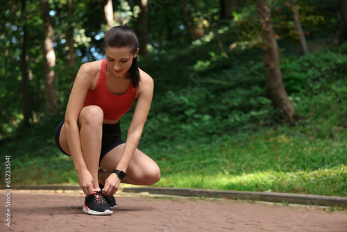 Beautiful woman in sportswear tying shoelaces in park. Space for text