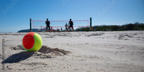 Doubles beach tennis game on the beach with blue sky and beach tennis ball in the foreground.