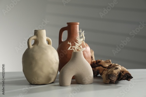 Clay flagons, vase, dried flowers and wooden snag on white marble table photo