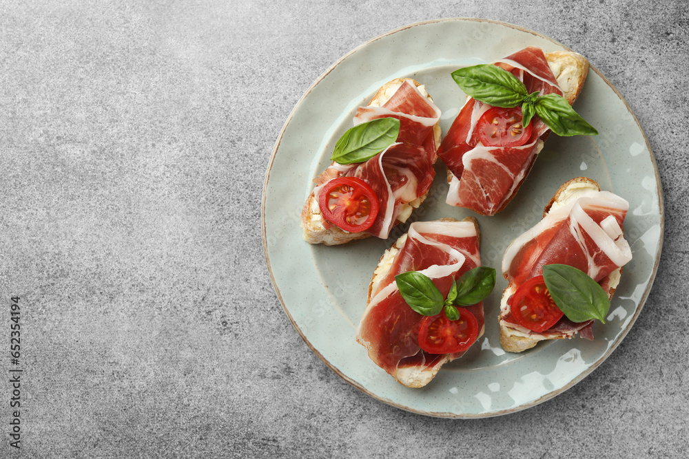 Tasty sandwiches with cured ham, basil and tomatoes on grey table, top view. Space for text Tasty sandwiches with cured ham, basil and tomatoes on grey table, top view. Space for text