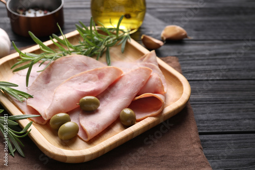 Slices of delicious ham with rosemary and olives served on dark wooden table. Space for text