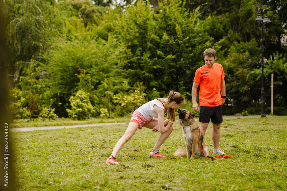 Obraz premium Couple doing workout while spending time in park with their dog