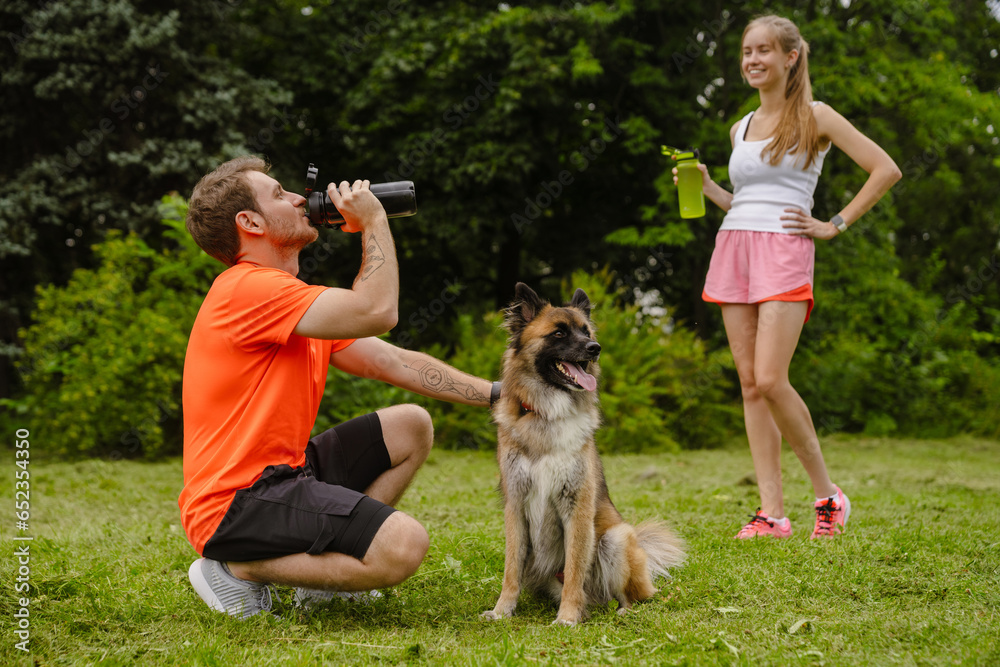 Couple drinking water while spending time with their dog in park