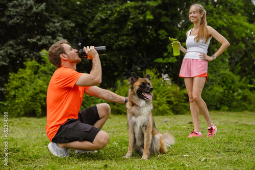 Couple drinking water while spending time with their dog in park